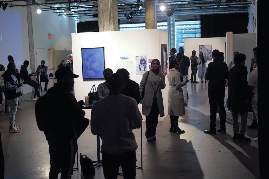 Guests gathered at a vernissage in low blue light, conversations around a framed blue portrait