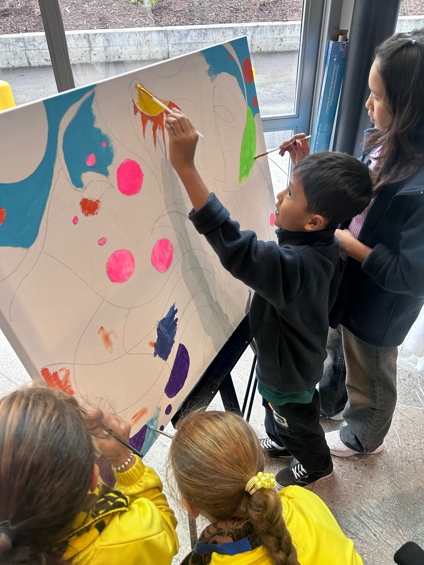 Young participants reaching up to add bright colors to a shared canvas