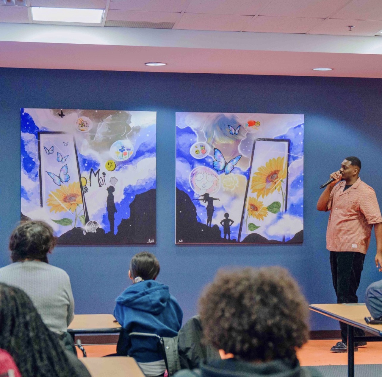 Dino speaking with a microphone in front of his paintings