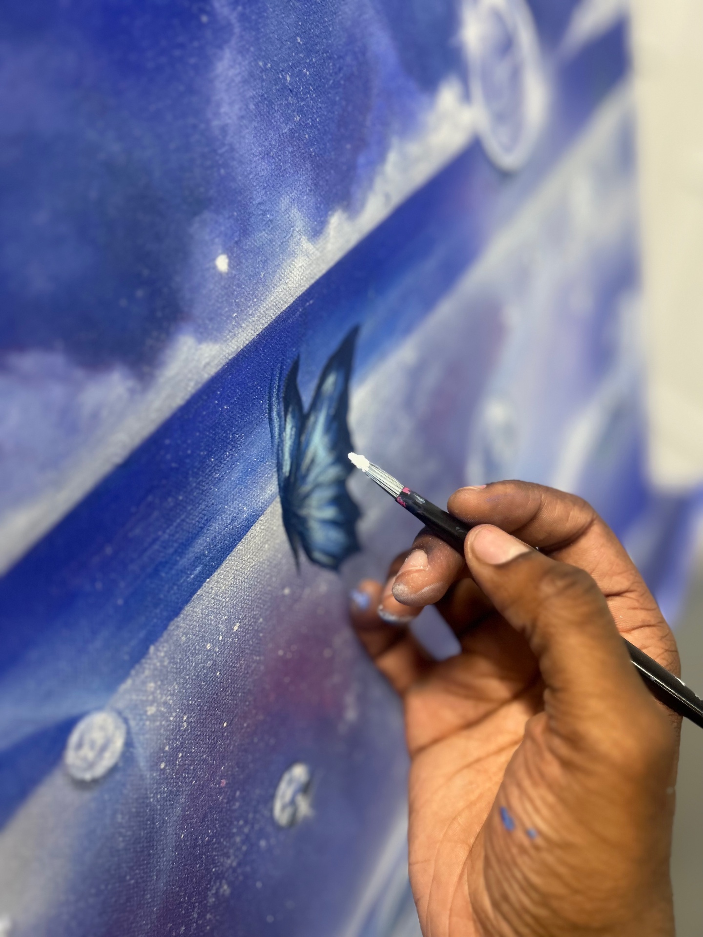 Close-up of a hand painting a delicate blue butterfly on a deep blue canvas