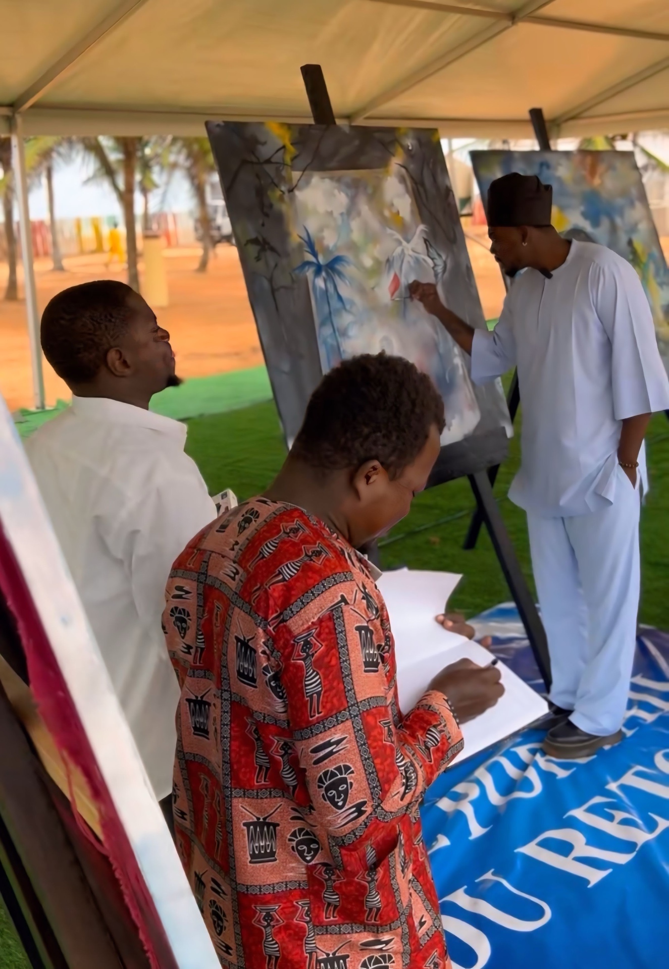 Live painting session under a tent in Benin, artist working on a canvas as guests sign the guestbook