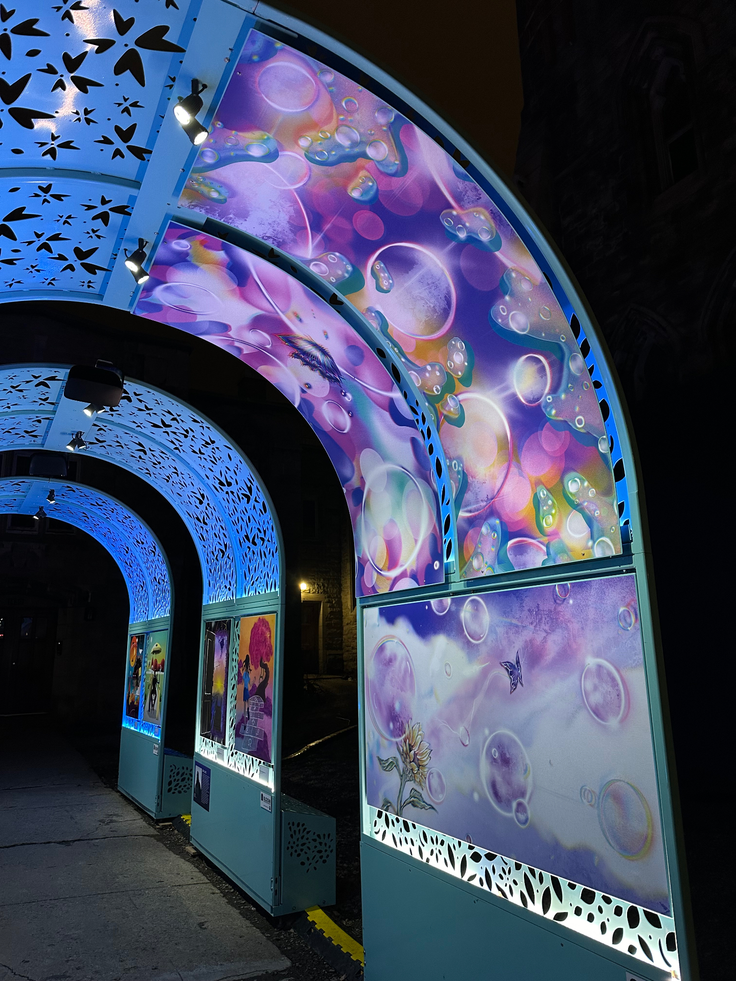 Illuminated outdoor arches displaying purple bubble murals at night