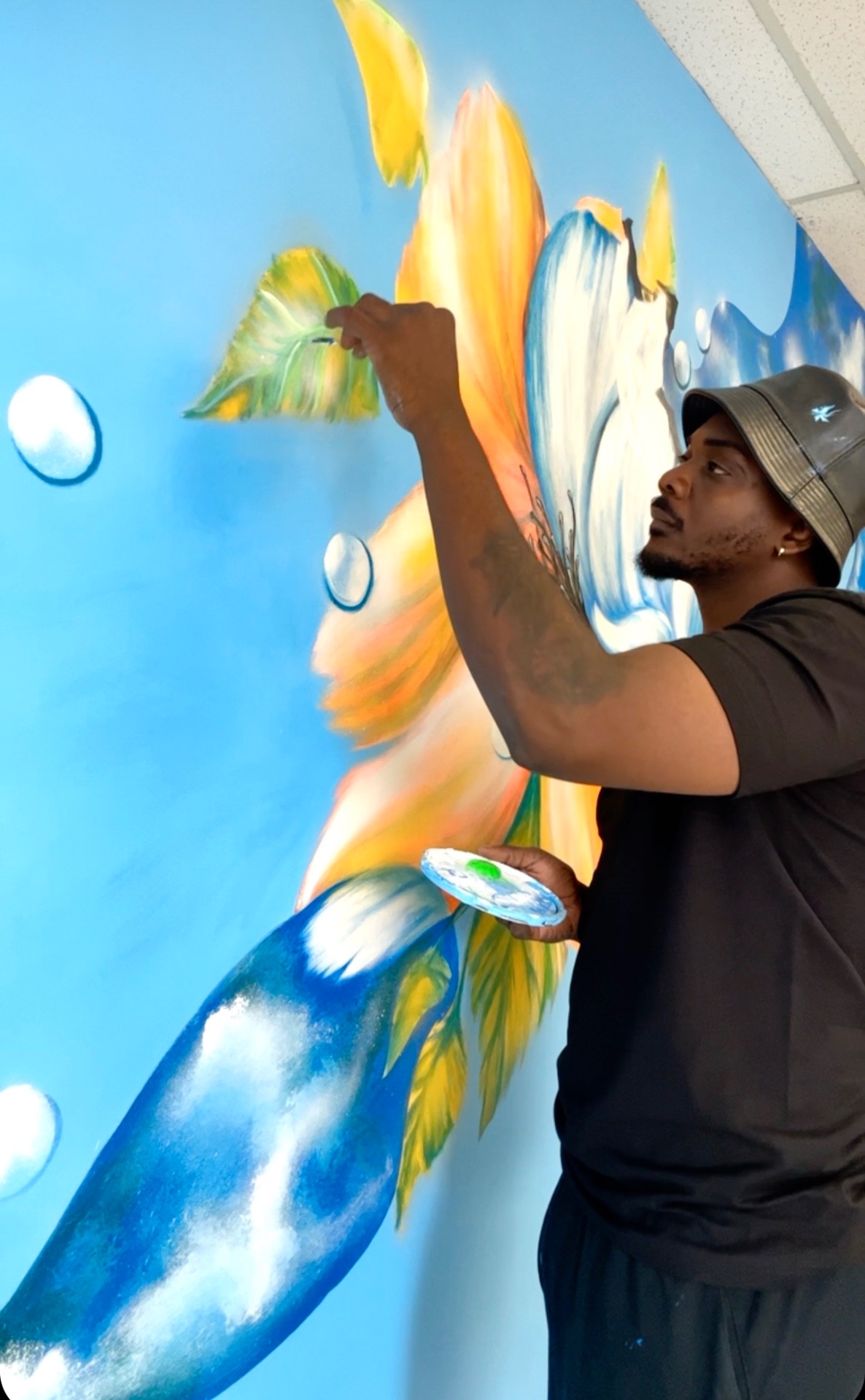 Dino painting a large orange and blue flower mural on a bright blue wall