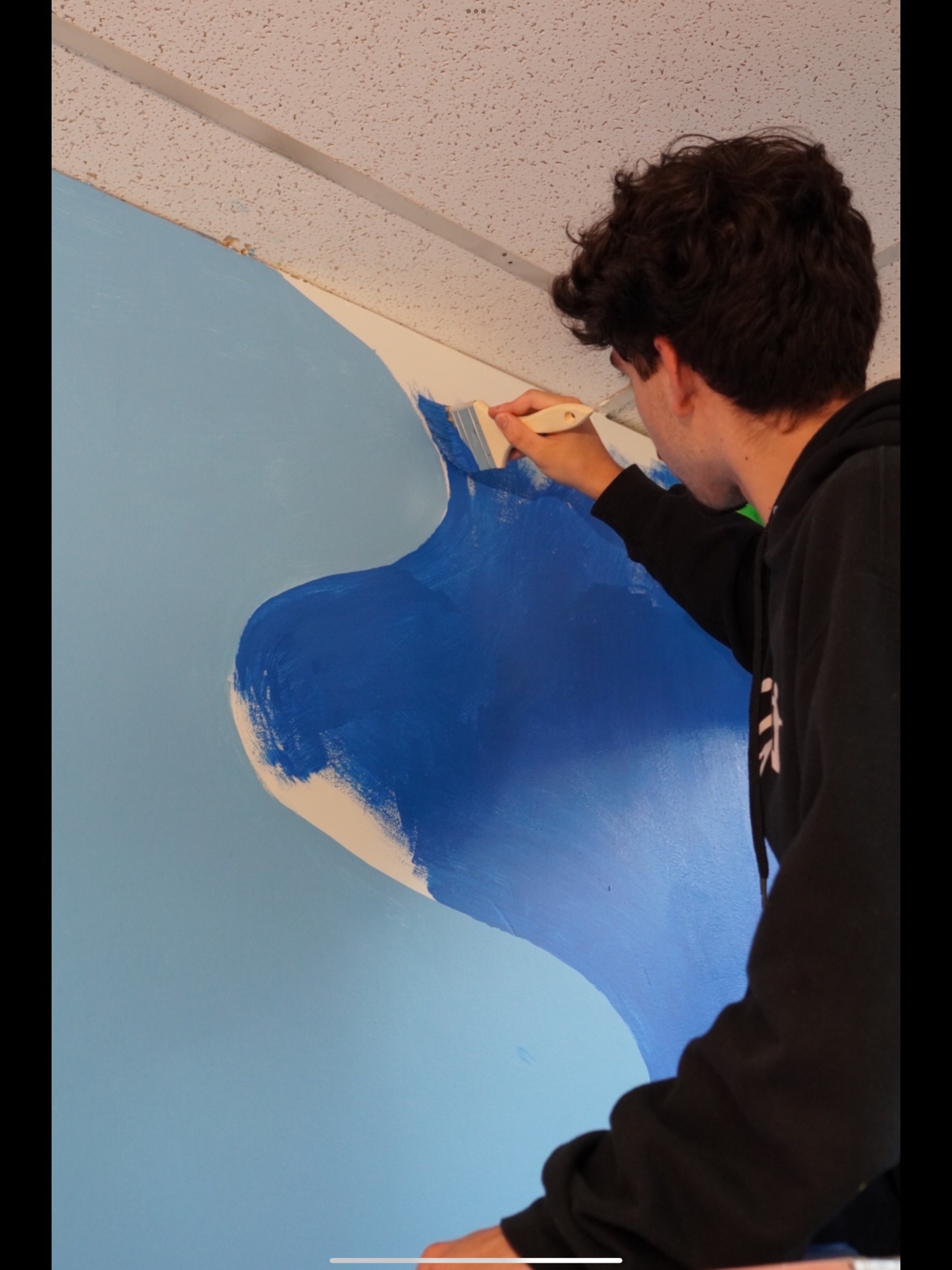 Young participant carefully painting a blue mural during a school co-creation workshop
